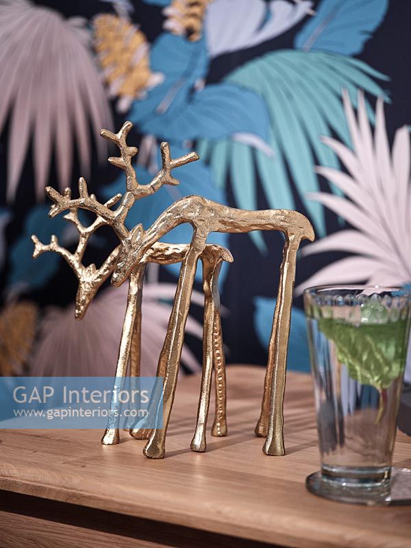 Small gold reindeer ornaments next to colourful wallpaper 