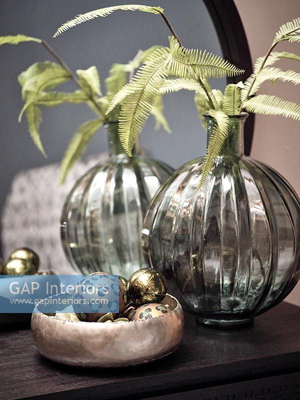 Foliage in vase next to metallic bowl of Christmas baubles 