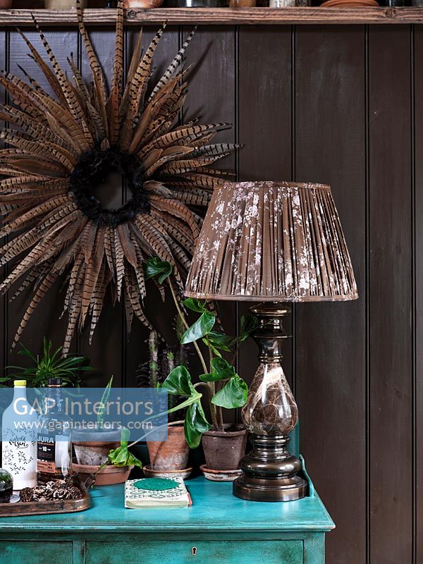 Feather wreath above painted chest of drawers and lamp