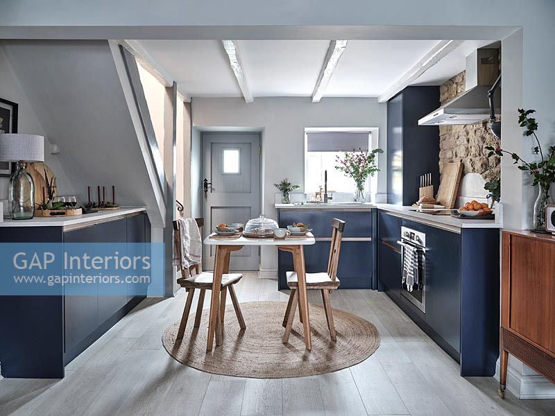 Small wooden dining table in centre of blue and white modern kitchen 