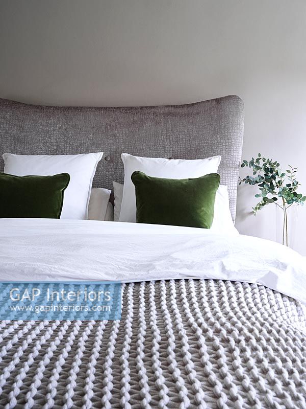 Grey bed and bedding with green cushion and plant