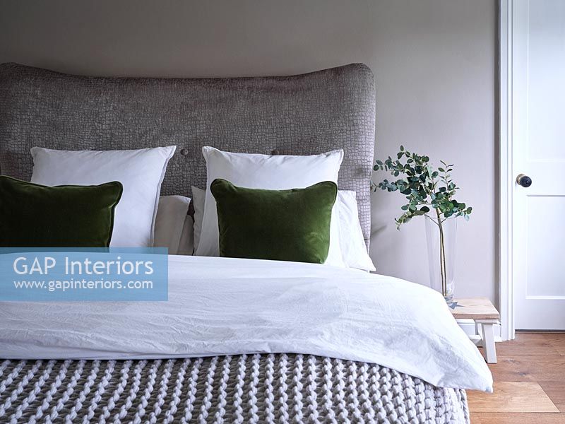 Grey bed and bedding with green cushion and plant