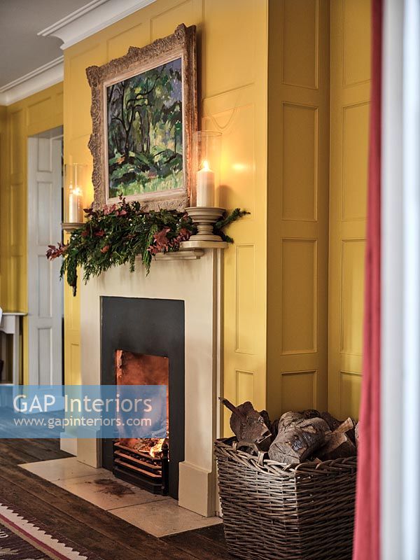 Christmas garland and candles on mantelpiece of lit fireplace 