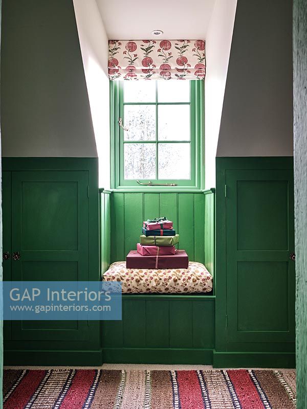 Wrapped gifts on tiny window seat with green painted panelled walls 