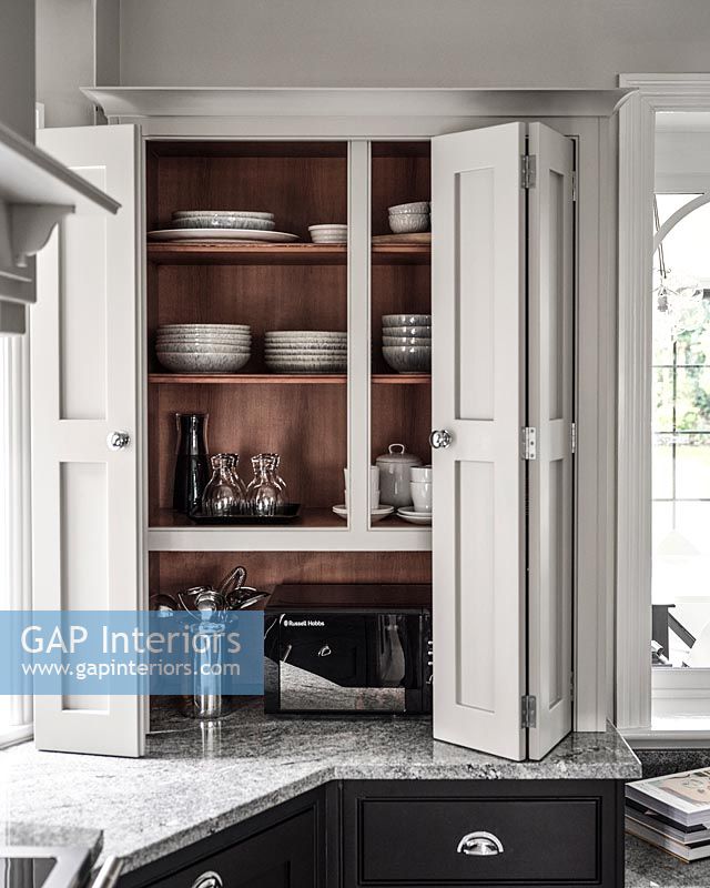 Modern kitchen unit - open cupboard doors revealing crockery storage 
