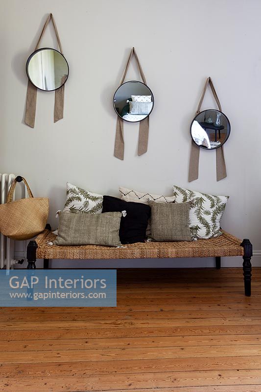 Row of matching mirrors above wicker bench seat with cushions 