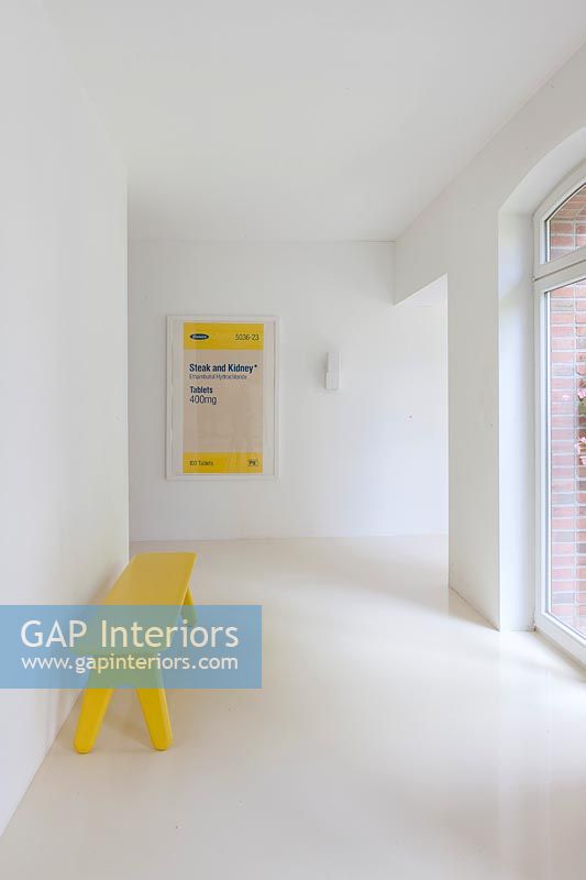 Contemporary white painted corridor with yellow artwork and bench