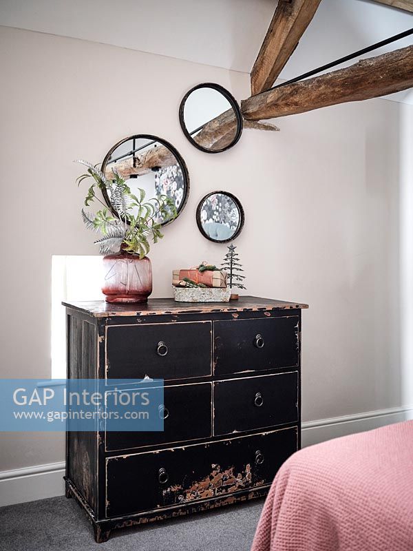 Black chest of drawers and display of round mirrors in country bedroom 