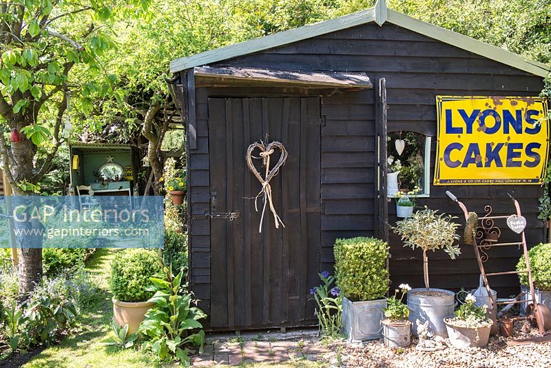 Black painted shed with vintage shop sign in cottage garden