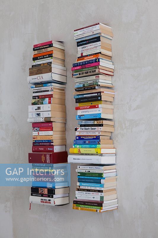 Tall towers of books on wall mounted floating shelves 