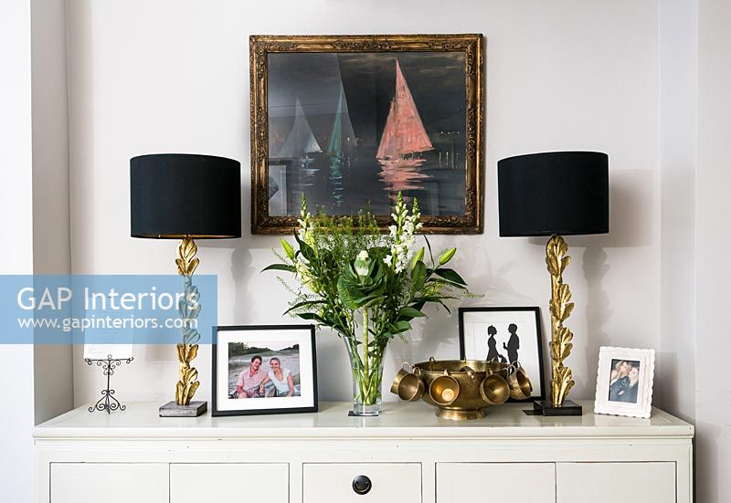 Vase of flowers on sideboard with lamps and artwork 