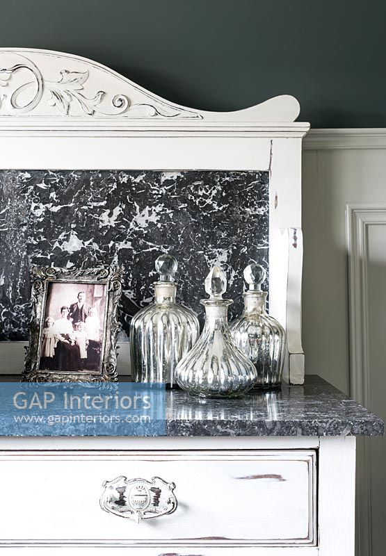 Decorative glassware on white painted chest of drawers with marble top