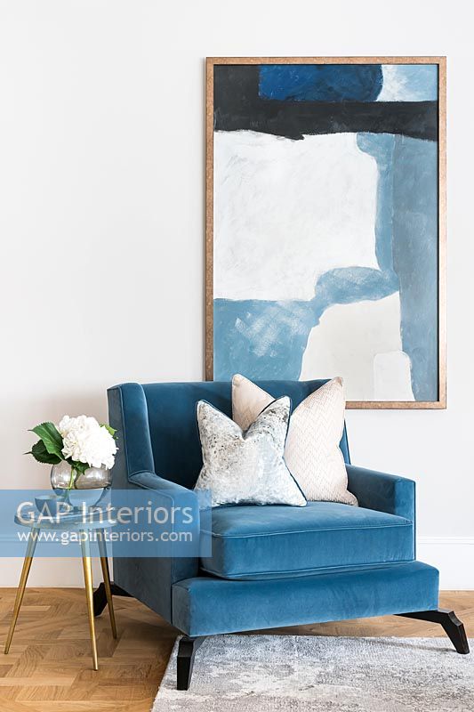 Blue modern armchair with large painting on wall behind 