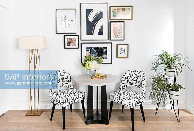 Modern table and chairs with display of framed artwork on wall 