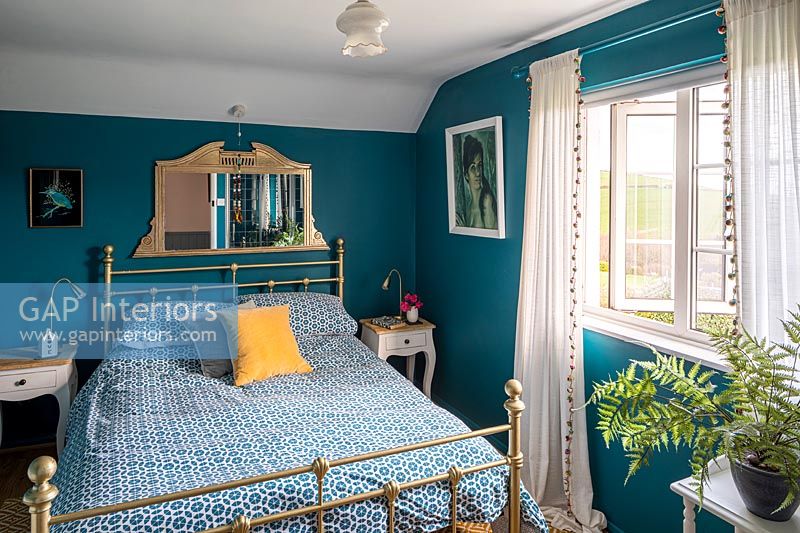 Teal painted walls in modern country bedroom with brass bed