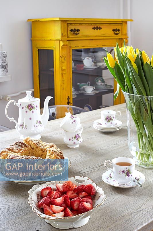Afternoon tea on dining table with yellow painted antique cabinet behind 