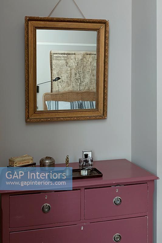 Gilded mirror over pink painted chest of drawers in bedroom 