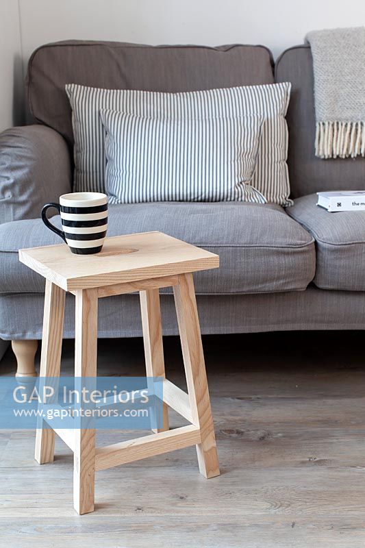 Small wooden stool used as side table next to grey sofa 