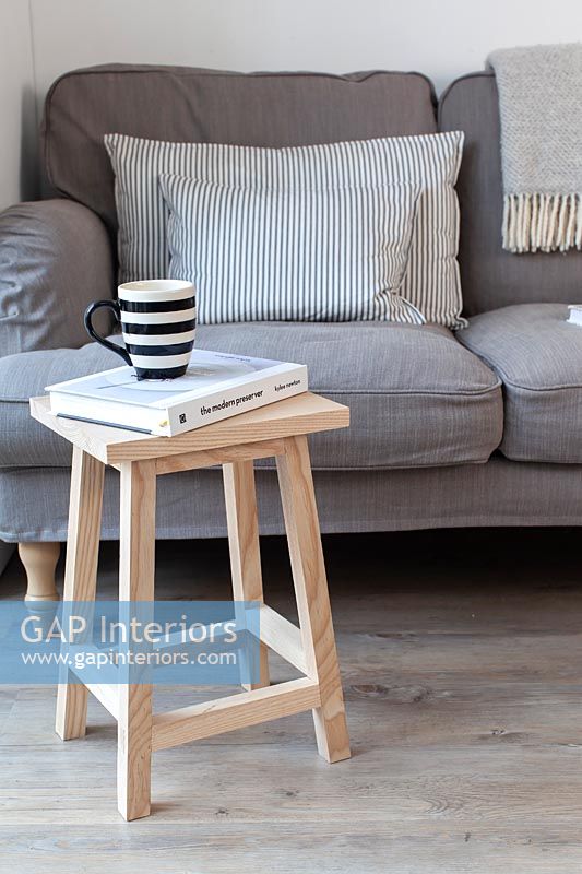 Small wooden stool used as side table next to grey sofa 