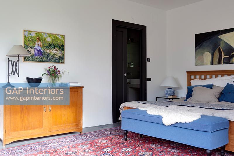 Modern bedroom with blue ottoman at end of the bed 