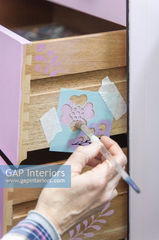 Woman using a stencil to add a subtle pattern on the sides of the drawers