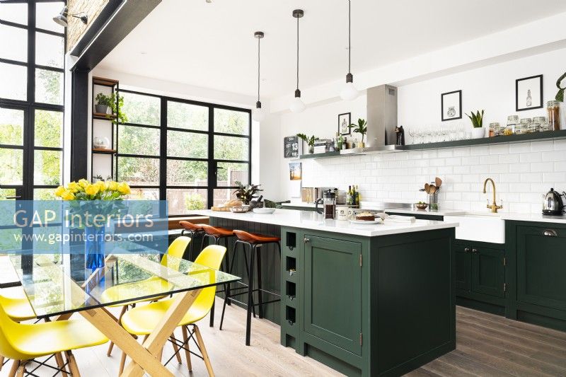 Contemporary kitchen extension with green cupboards, island, crittall style windows and yellow dining chairs