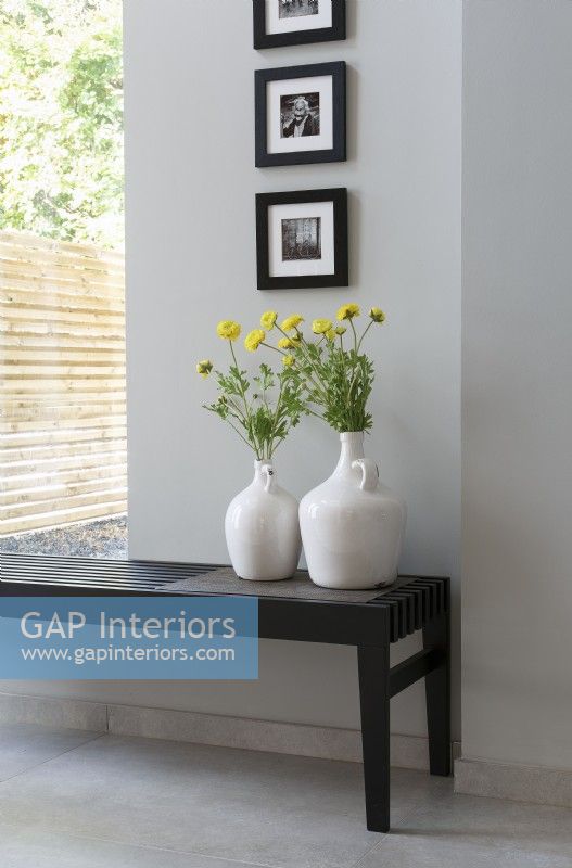 Large white jug vases with yellow flowers against grey wall