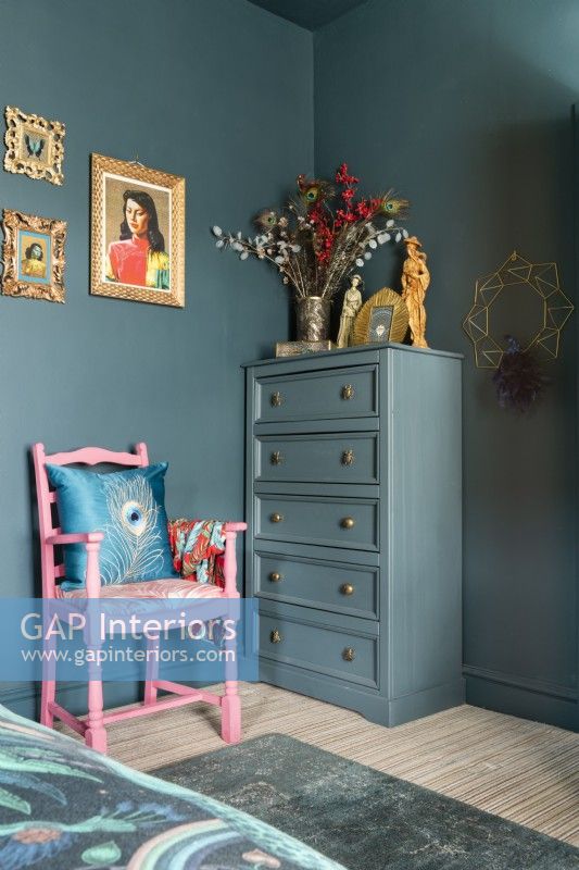 Painted tall boy chest of drawers in the corner of a bedroom with pink painted armchair
