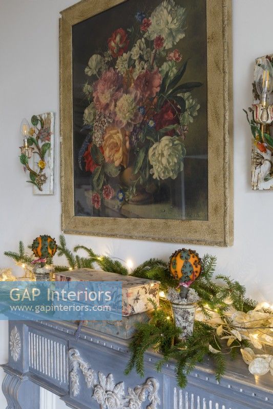Mantlepiece decorated for christmas with painting of vase of flowers above