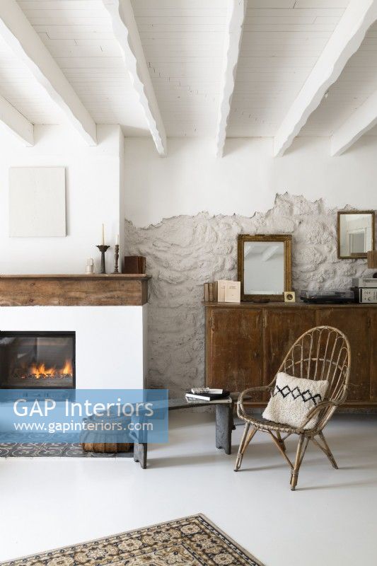 Wicker chair and old wooden sideboard next to lit fireplace