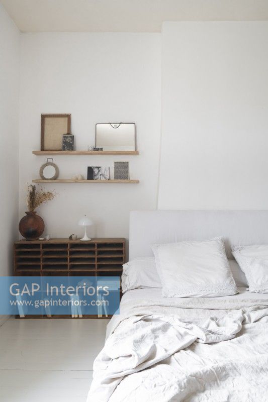 Wooden shelving unit next to bed in white country bedroom
