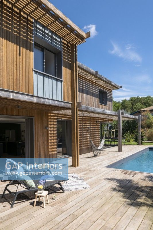 Recliners on decking next to swimming pool - modern wooden house