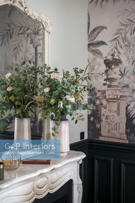 Flower arrangement on marble mantelpiece next to wallpapered wall