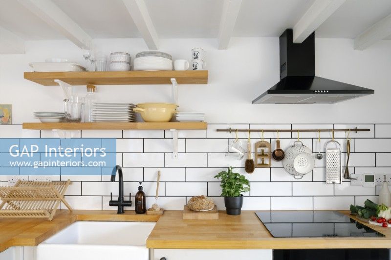 Contemporary L-shaped Kitchen with white subway tiles and wooden work surface. Wooden Shelving holds plates and crockery. 