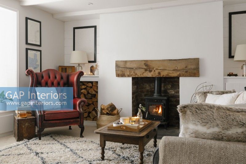 Contemporary open plan living room in a Cornish cottage. Featuring wood burner and red leather wingback armchair.