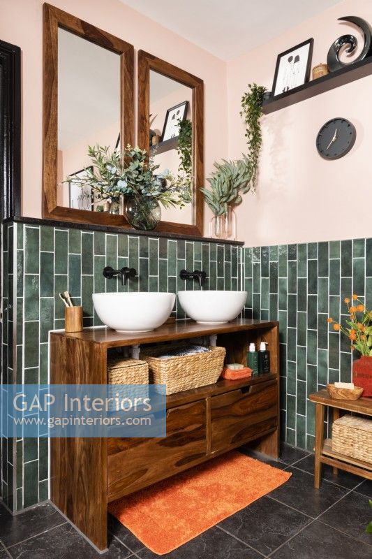 Twin round white sink bowls on a wooden unit in a green tiled bathroom
