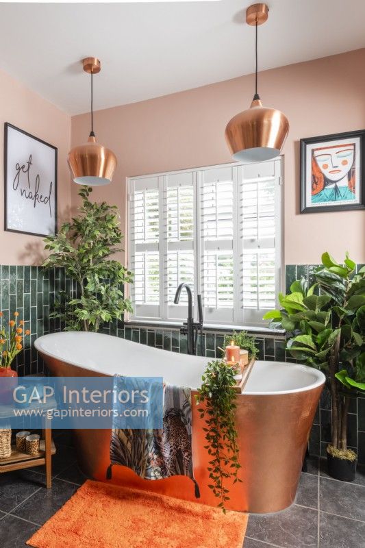 Free standing copper covered bathtub next to window with plantation shutters