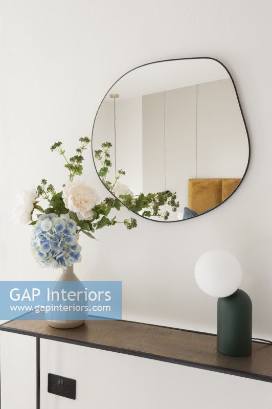 Mirror above a console table with vase of flowers and lamp