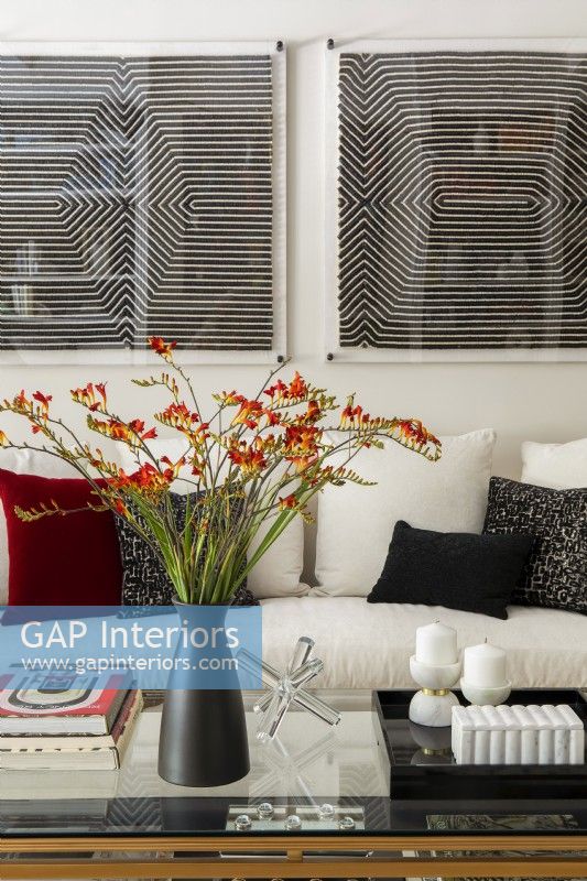 Flower arrangement on glass coffee table in front of white sofa with cushions.