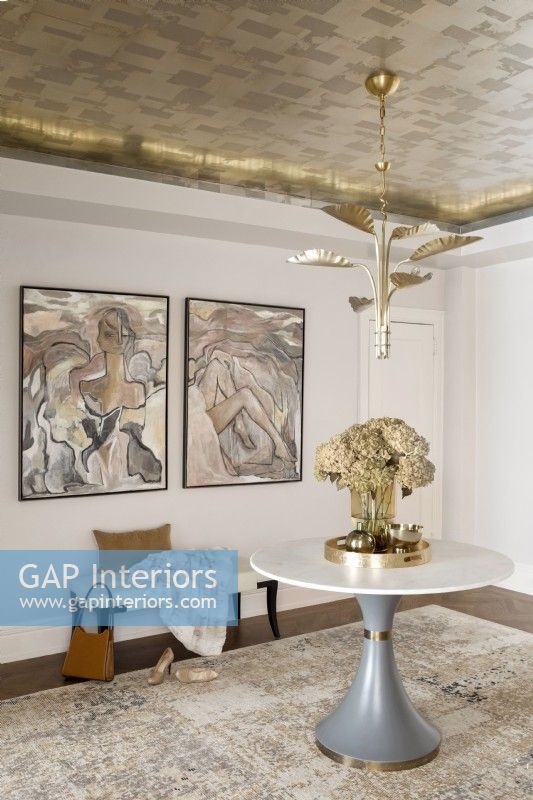 Room details with metal leaf wallpaper on ceiling decorated with pedestal table, bench and artwork.