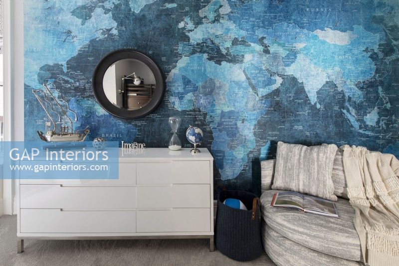 White chest of drawers in front of feature wall with a vinyl world mural.