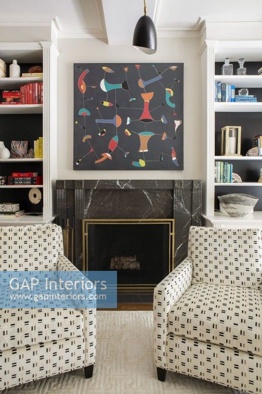 Two patterned armchairs in front of marble fireplace. 