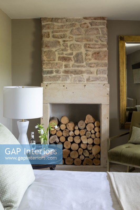 Wood stored in fireplace of contemporary bedroom.  Stone fireplace and pale green colour scheme