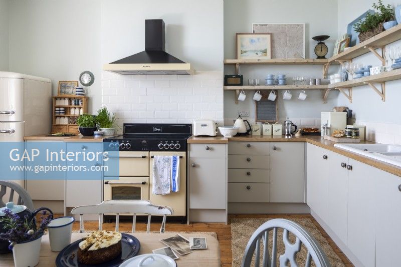 Simple contemporary kitchen with wooden shelving, beige coloured units an Aga cooker and a wooden worktop