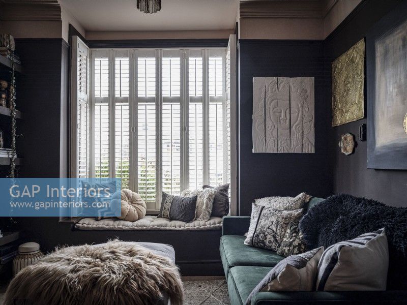 Dark living room with velvet sofa, window seat and plantation shutters