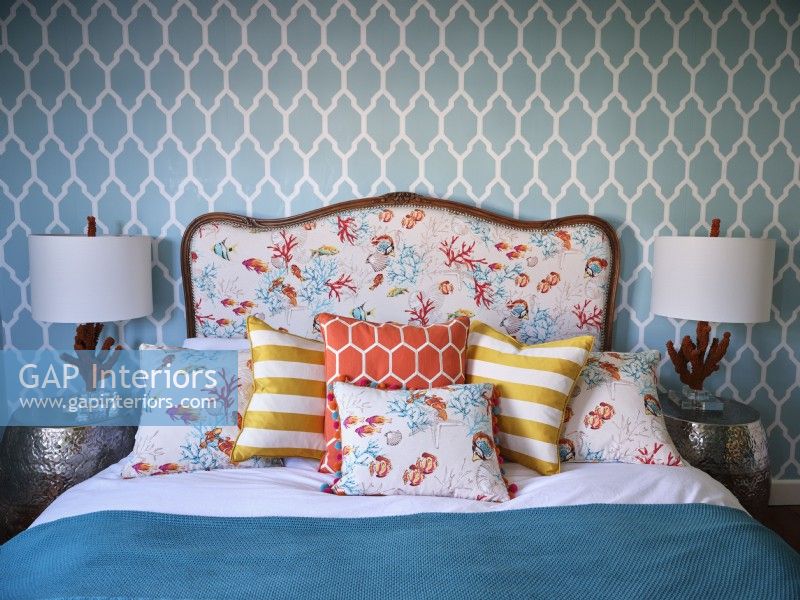 Colourful coastal bedding on upholstered bed next to coral sculptured lamps
