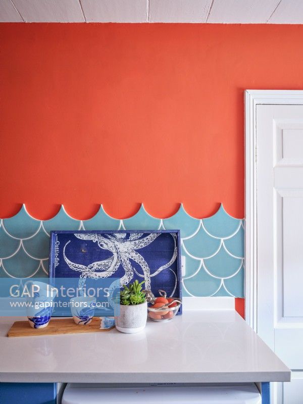 Coastal inspired tray and cups in front of sea blue tiles and a red wall 