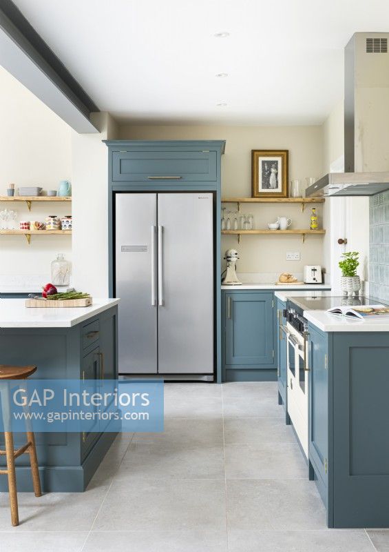 Modern classic kitchen with blue cupboards, island, open shelves, concrete floor tiles and integrated fridge.
