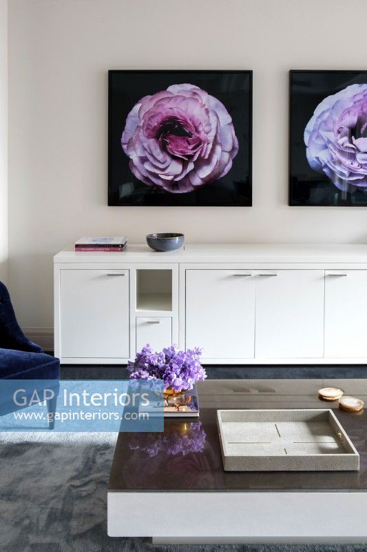 Modern living room details with long white credenza decorated with photographs of flowers on wall.