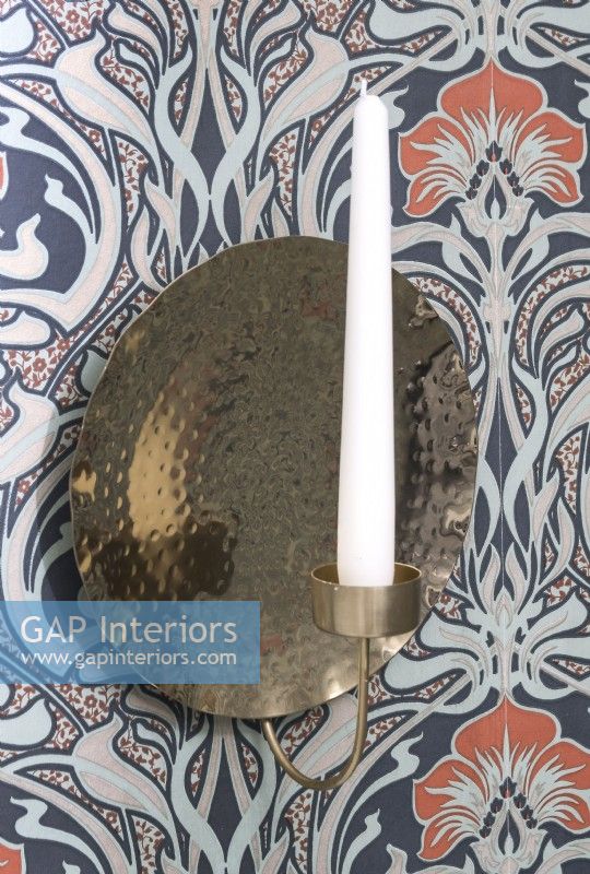 Wall mounted gold candle holder on patterned wallpapered wall